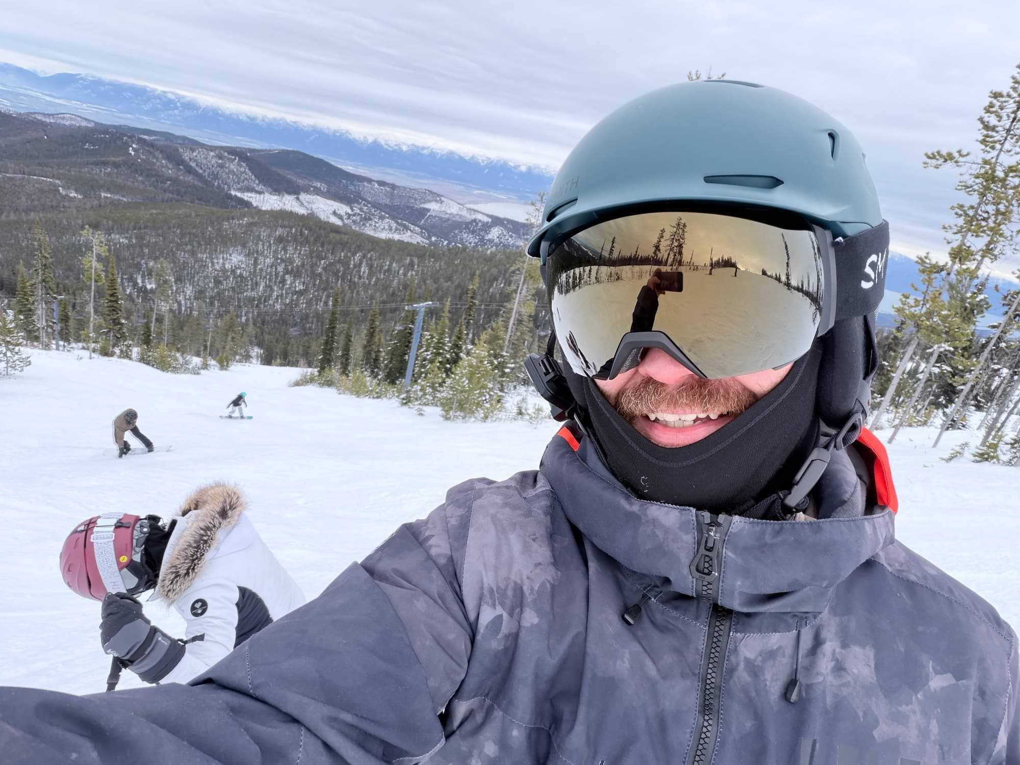 A groomed ski run with forested slopes and mountain ridges in the distance.